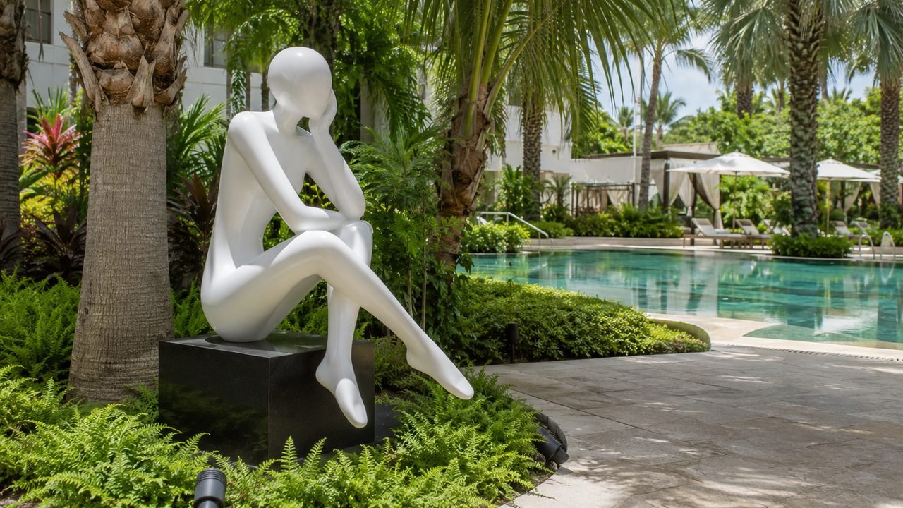 Glossy white modern figurative fiberglass sculpture beside a resort pool with tropical garden in the UAE